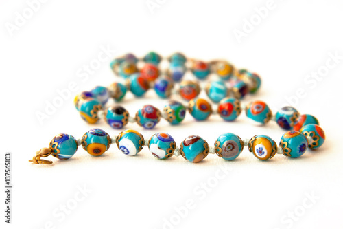 Original Murano glass beads with floral pattern necklace isolated. Venetian traditional colorful millefiori glass jewelry. String of blue  beads, focus on the first row