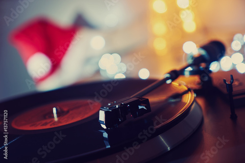 Image of Christmas. Gramophone playing a record. Gramophone with vinyl record on a background of Christmas decorations, cap and lights. Bright background for the design 