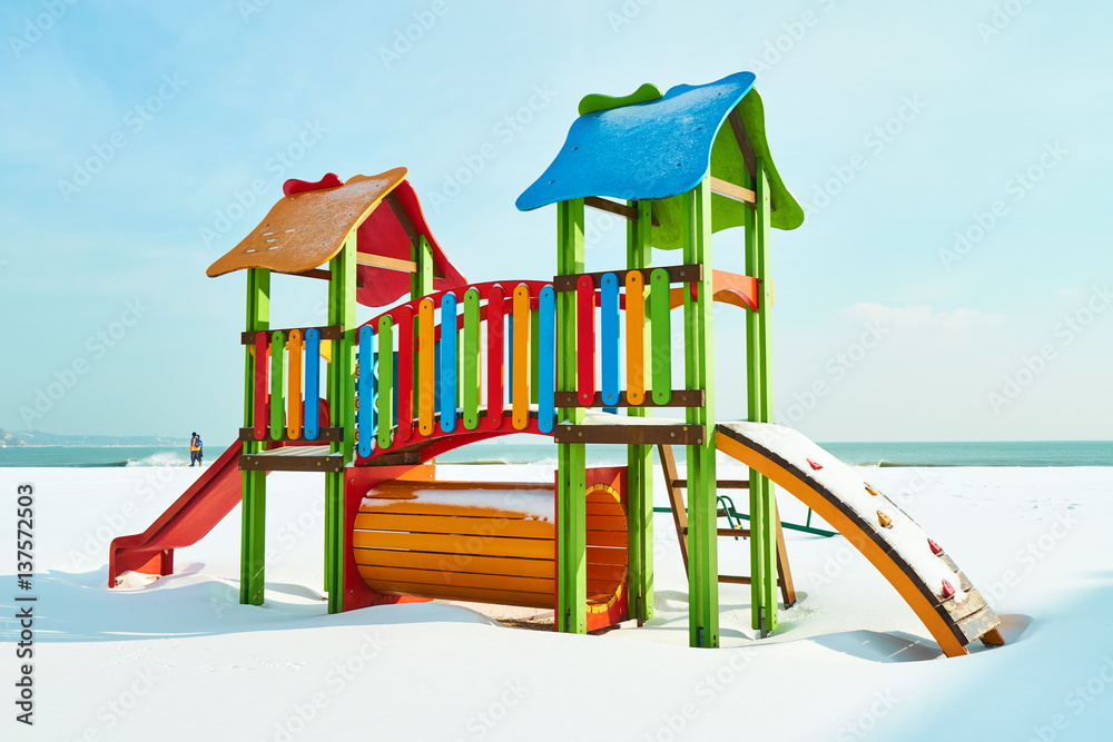 Bright children's playground in the snow on the beach in winter sunny day
Bright children's playground in the snow on the beach in winter sunny day