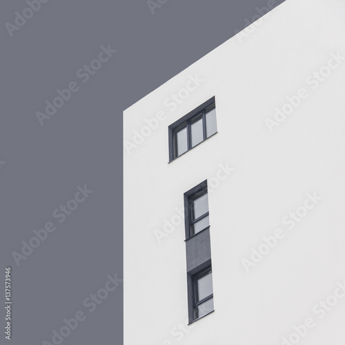 White apartment block with dark grey windows under abstract grey sky. Isolated. Quadrate photo. Bottom view. Concept: life, couple, family, kids, independence, abstract, minimalism. photo