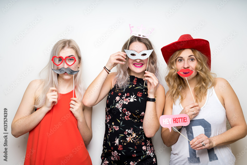 three happy young ladies girls strike a pose on white background photo booth with party props