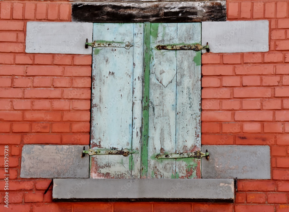 Close up of red brick wall with window and closed wooden shutters Close up of red brick wall with window and closed wooden shutters