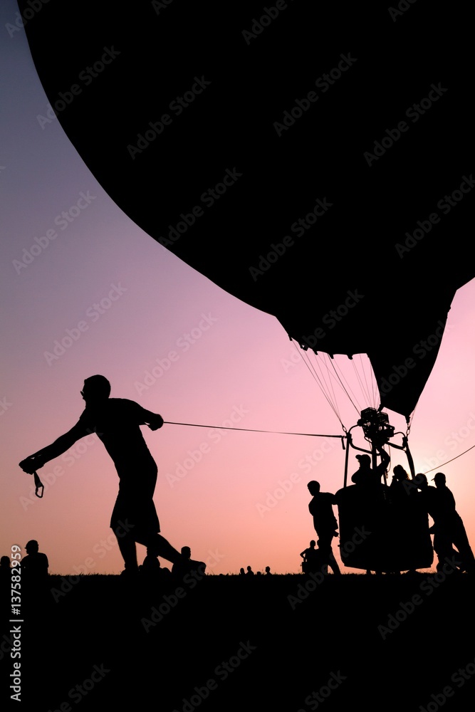 Silhouette of man pulling an hot air balloon by a rope with pink