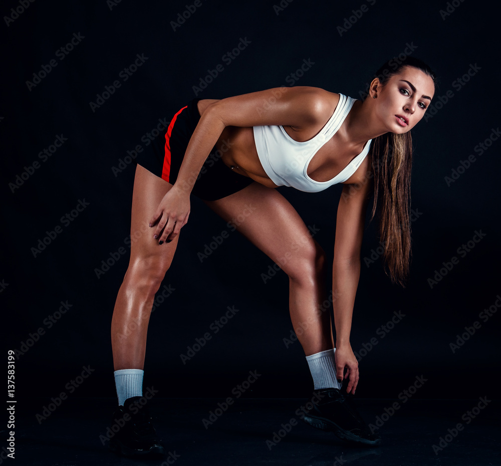 Athletic young woman doing a fitness workout against black background. Sporty woman in sportswear with perfect fitness body.