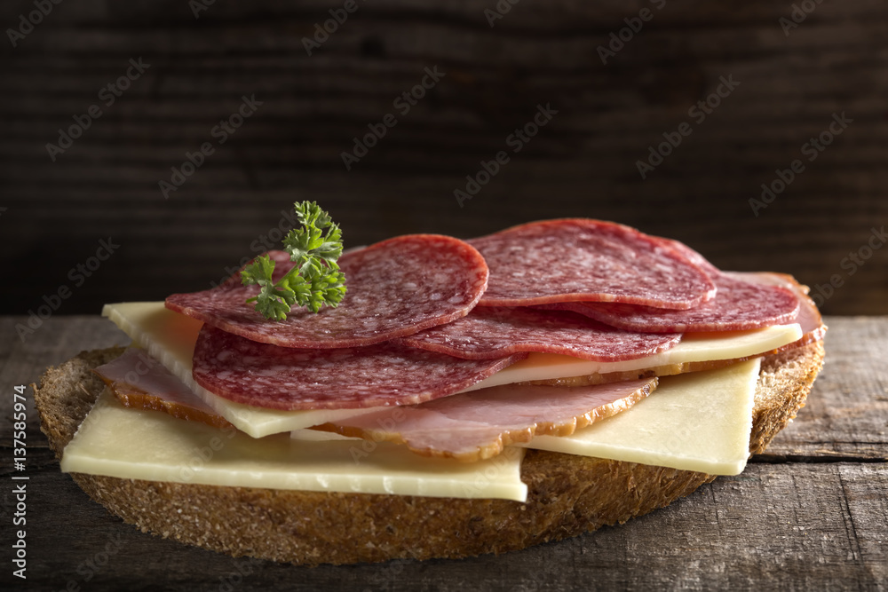 Open sandwich made from cheese, ham and Italian salami on wood