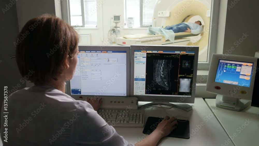 Doctor sitting at the monitor and controling medical MRI examination of patient Doctor sitting at the monitor and controling medical MRI examination of patient