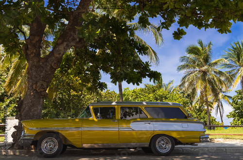 Amerikanischer gold gelber Oldtimer parkt in Varadero nahe des Strandes unter Palmen in Kuba - Serie Kuba Reportage © mabofoto@icloud.com
