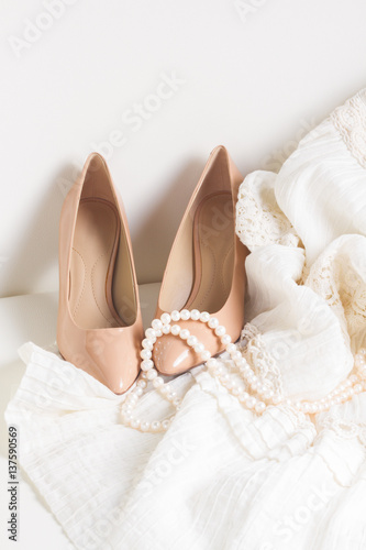 Female accessories - dress, shoes on white leather chair still life, vertical image