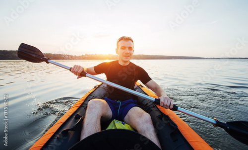 man floating on lake in a kayak at fantastic sunset.