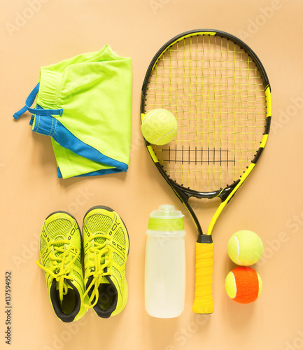 Tennis stuff on cream background. Sport, fitness, tennis, healthy lifestyle, sport stuff. Tennis racket, lime trainers, tennis ball, lime athletic shorts, sports bottle. Flat lay, top view.