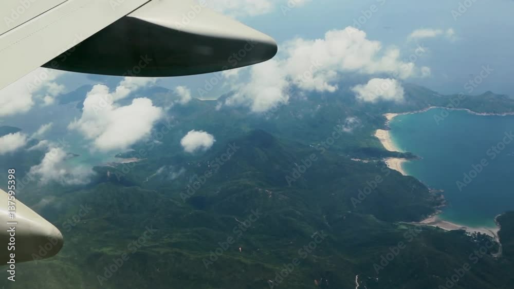 Traveling by air. Aerial view with many clouds of the Hong Kong Mountain and ocean from above, as seen through an airplane window-Dan Traveling by air. Aerial view with many clouds of the Hong Kong Mountain and ocean from above, as seen through an airplane window-Dan