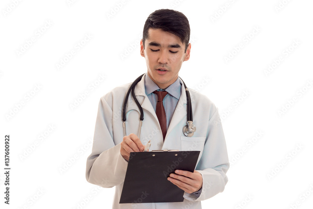 portrait of young handsome brunette man doctor in white uniform posing on camera with stethoscope on his neck make notes isolated on empty background portrait of young handsome brunette man doctor in white uniform posing on camera with stethoscope on his neck make notes isolated on empty background