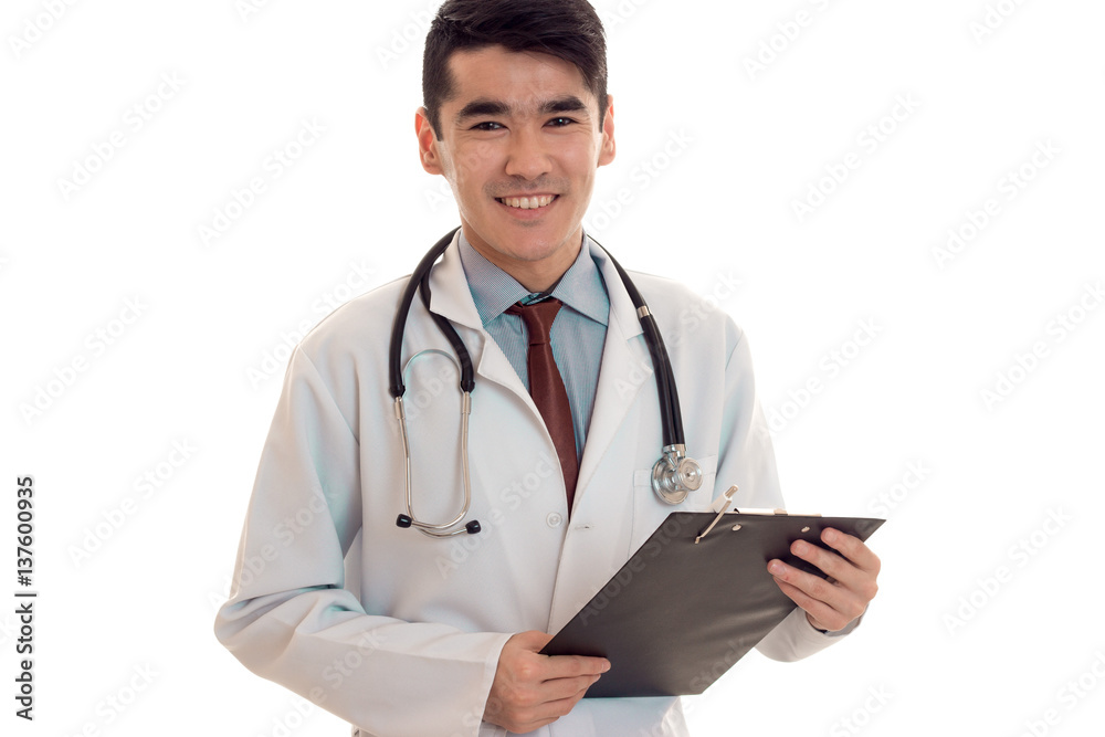 portrait of young cheerful brunette man doctor in white uniform smiling on camera with stethoscope on his neck make notes isolated on empty background portrait of young cheerful brunette man doctor in white uniform smiling on camera with stethoscope on his neck make notes isolated on empty background