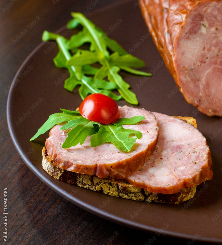 Smoked sausage, ham with red tomatoes and lamb's lettuce on a dark brown plate