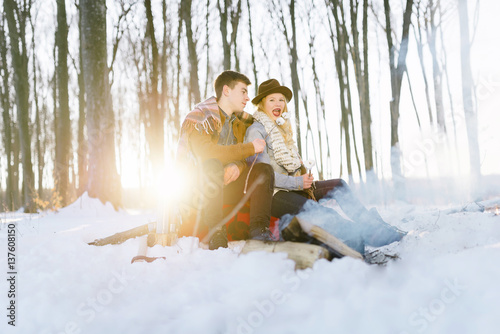  stylishly dressed young couple, sitting near the fire in the winter forest