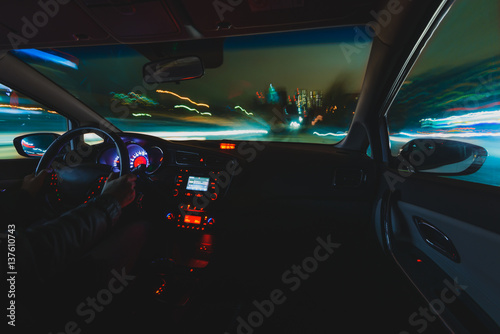 hands on the wheel a car moves at fast speed at the night. Blured road with lights with car on high speed. Car speed night drive on the road in city