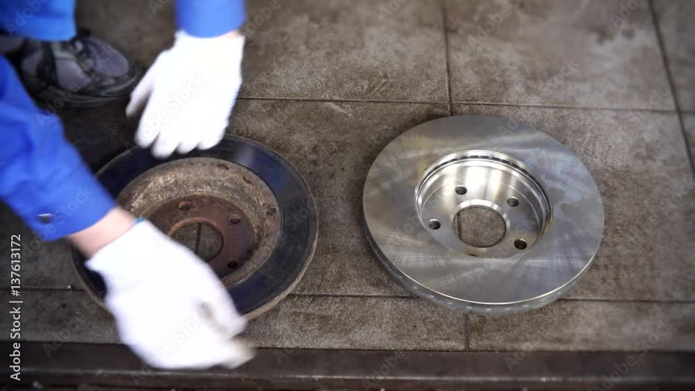 Mechanic man hands compare old worn brake disk with new object. Mechanic man hands compare old worn brake disk with new object.