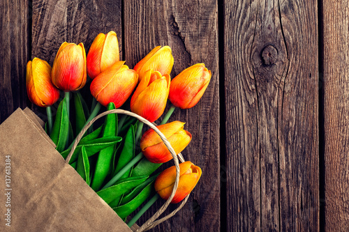 Fototapeta Naklejka Na Ścianę i Meble -  Bouquet of tulips in a paper shopping bag on a wooden background, concept of discounts and sales on the Women's Day or Mother's Day or Easter