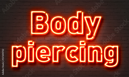 Photos Body piercing neon sign on brick wall background.