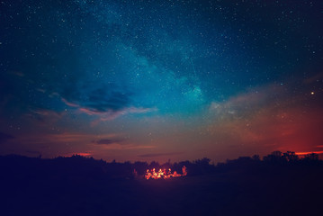 Camping fire under the amazing blue starry sky with a lot of shining stars and clouds. Travel recreational outdoor activity concept.