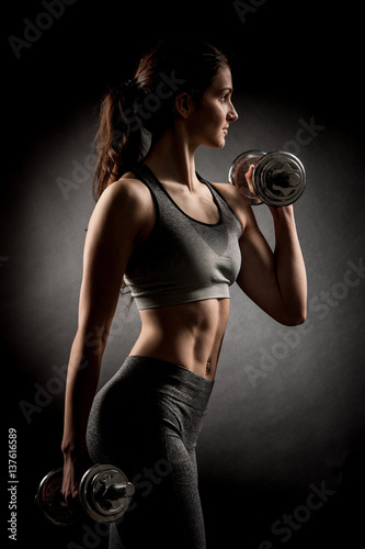 Atractive fit woman works out with dumbbells as a fitness conceptual over dark background