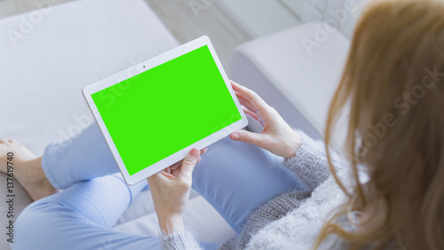Woman at home relaxing reading on the tablet computer with pre-keyed green screen