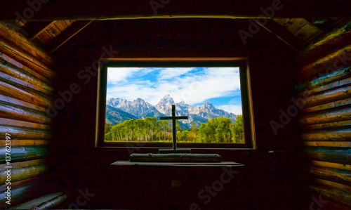 Grand Teton Mountains view through the window of a church with a cross.  Grand Tetons National Park, Jackson Hole, Wyoming, USA.