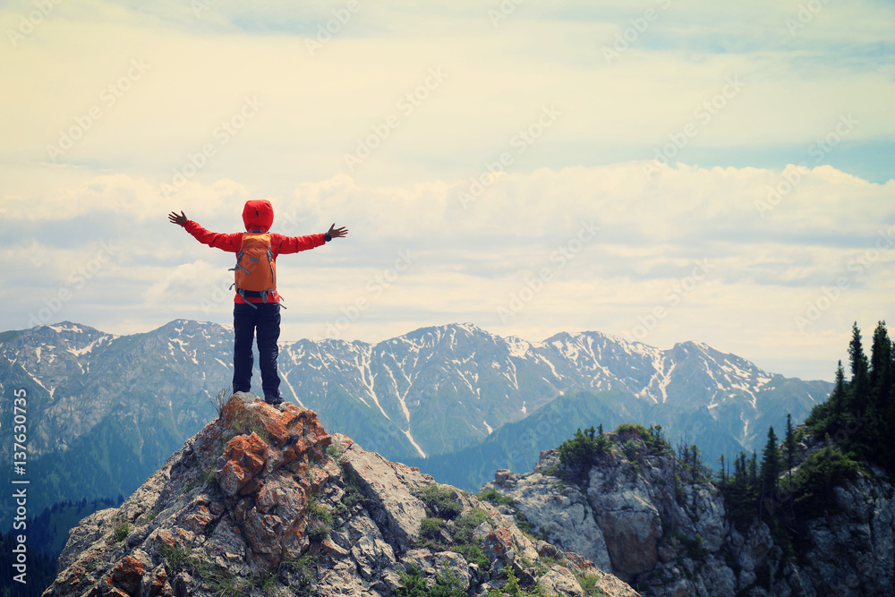 successful woman backpacker hiking on mountain peak cliff