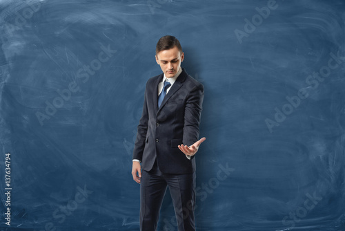 Businessman on blue chalkboard background holding one hand out and looking at it. photo