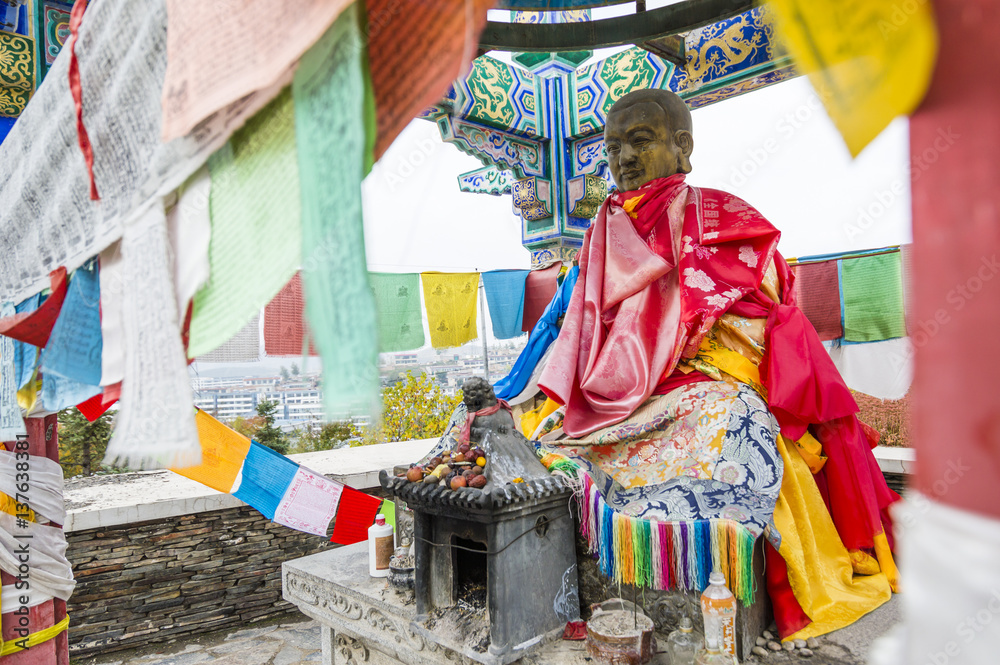 Buddha statue with tibetan prayer flags around on the street near Kumbum Monastery in Lusar, Qinghai province, China