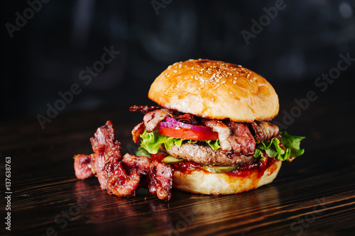 Burger with bacon, meat, tomato and lettuce   on wooden background. Close up