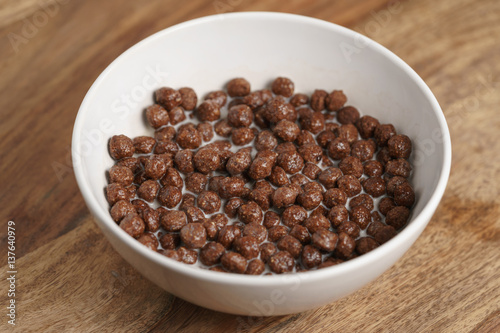chocolate cereal balls with milk in white bowl for breakfast on wooden table