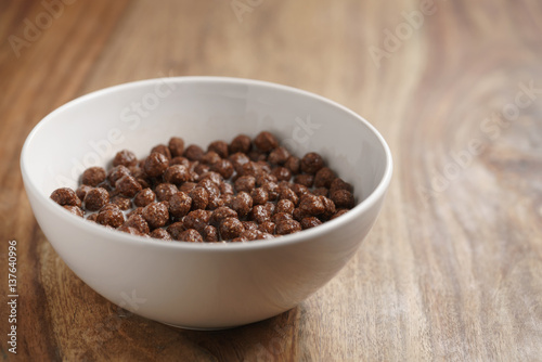 chocolate cereal balls with milk in white bowl for breakfast on wooden table