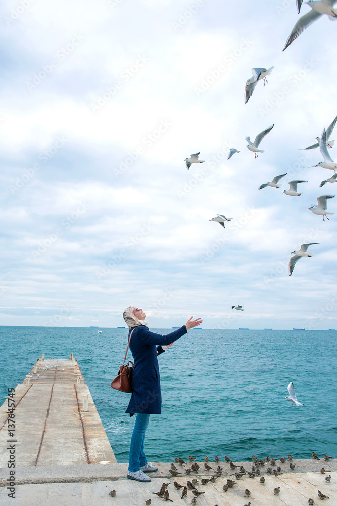 blonde woman feeding seagulls in cloudy autumn day on the sea coast 