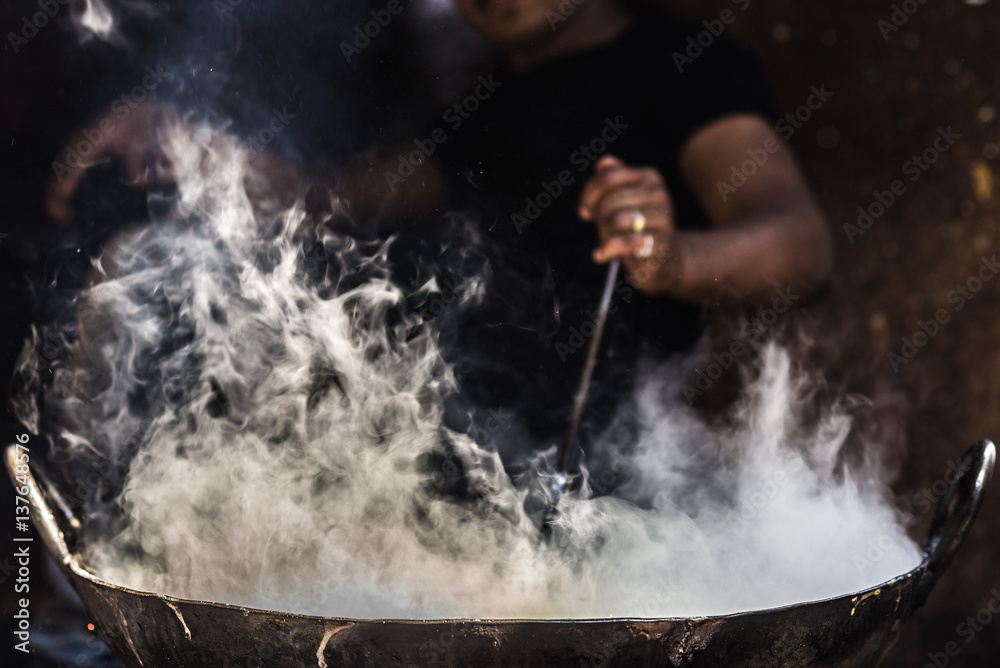 Obraz premium Unrecognizable man cooking in fatiscent big pan or wok in a small street food stall. White smoke coming out from the pan, hand and arm only visible. Street food in India.