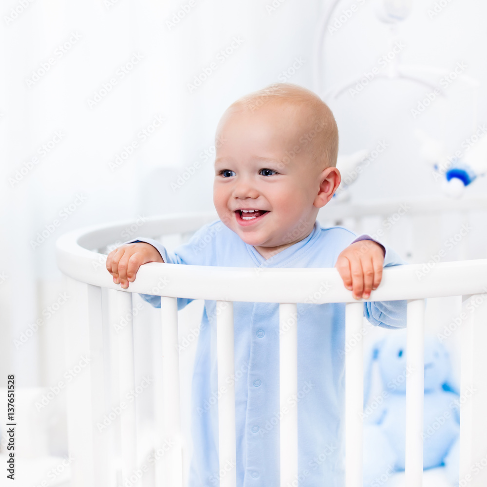 Baby boy standing in bed in white nursery Baby boy standing in bed in white nursery