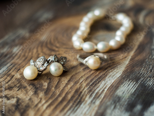 Macro of beautiful pearl earrings and Bride ring on wooden background.