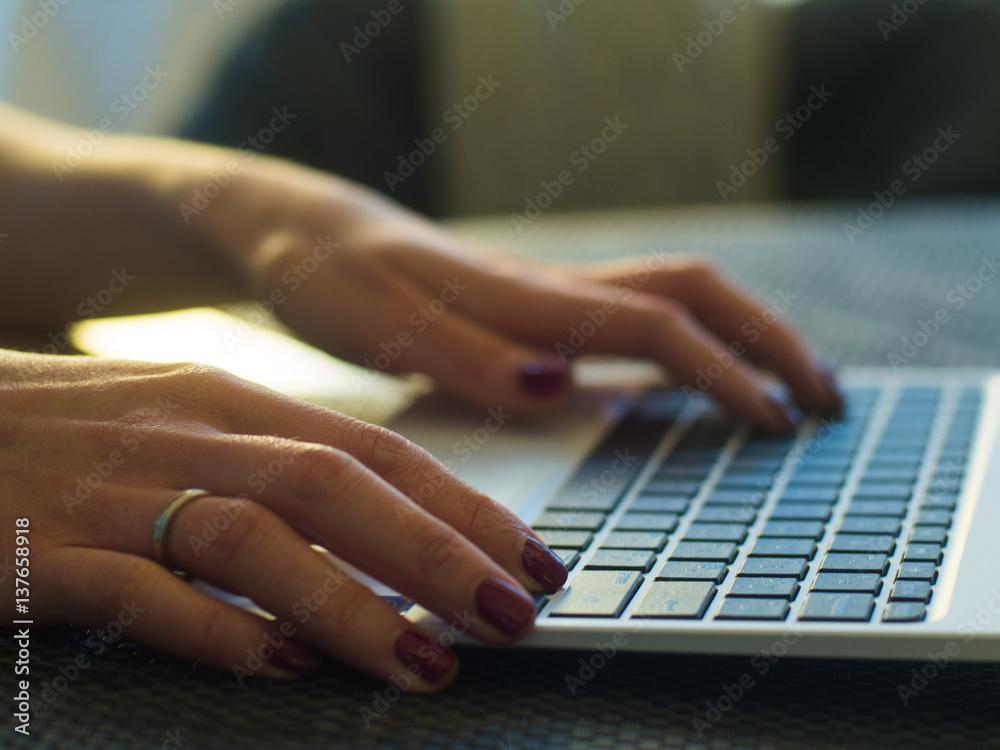 Woman's hands typing on laptop keyboard in interior, side view of businessman using computer in cafe