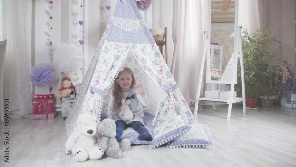Little cute girl with blond hair sitting in a toy house surrounded by ...