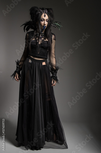 Young woman in black fantasy costume with feathers on dark background © FlexDreams
