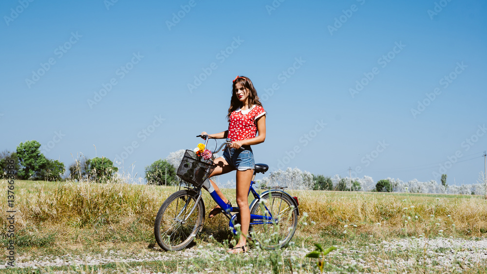 Young pinup woman cycling in fields under bright blue summer sky copy space image