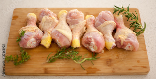 Chicken drumsticks on a cutting board with fresh rosemary and thyme. 
