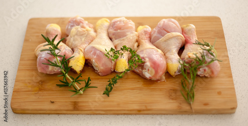 Chicken drumsticks on a cutting board with fresh rosemary and thyme.