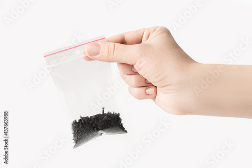 Hand holding Plastic transparent zipper bag with halfblack tea isolated on white, Vacuum package mockup with red clip. Concept. photo