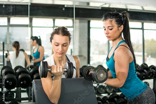 Young female friends doing exercises with weights in gym.