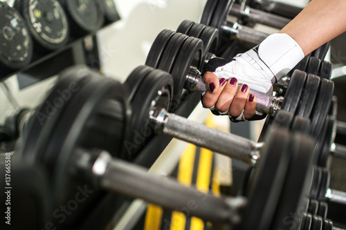 Hand of a female hand taking a dumbbell out of set of black weights.