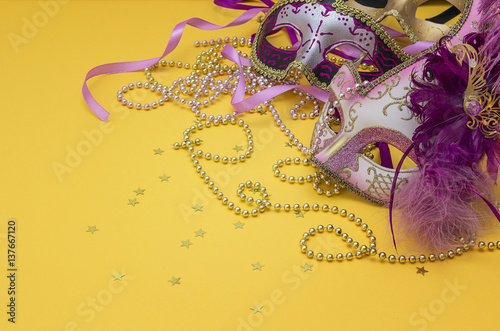 Purple carnival masks and golden beads on a yellow background. Space for text.