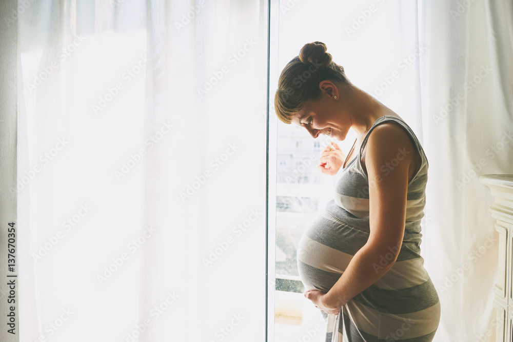 Young beautiful pregnant woman standing near window at home Young beautiful pregnant woman standing near window at home