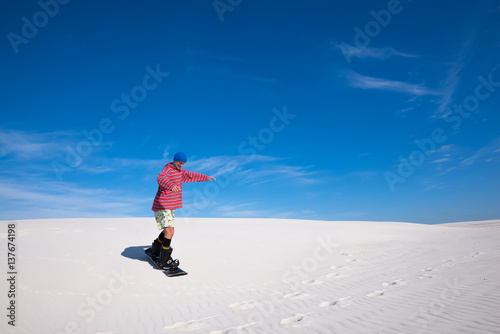 Man in colorful shirt training to snowboard on sand