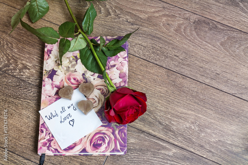 Rose with ribbon and message card on a book. Valentines Day background